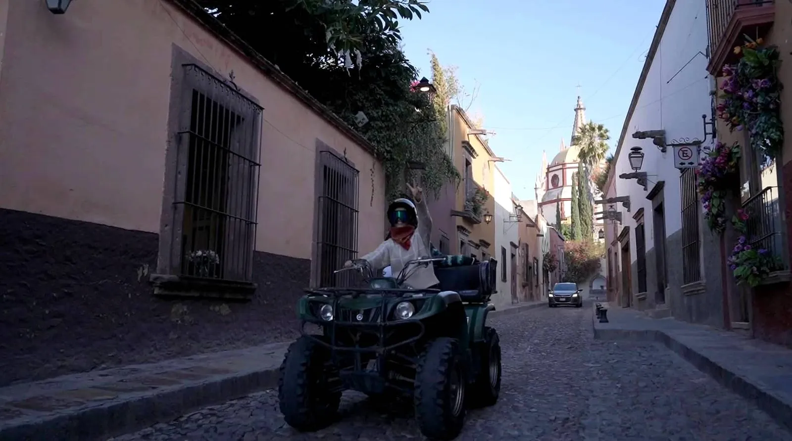 Single rider driving green quad through city street on ATV tours Person wearing a helmet riding a green quad down a narrow cobblestone street past colonial buildings on ATV tours.