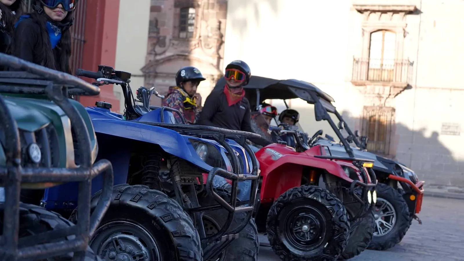 Getting ready for the ultimate adventure with Rzr rentals and ATVs. Close-up of a group of smiling people wearing helmets and safety goggles, standing next to a row of parked ATVs and Rzr rentals vehicles.